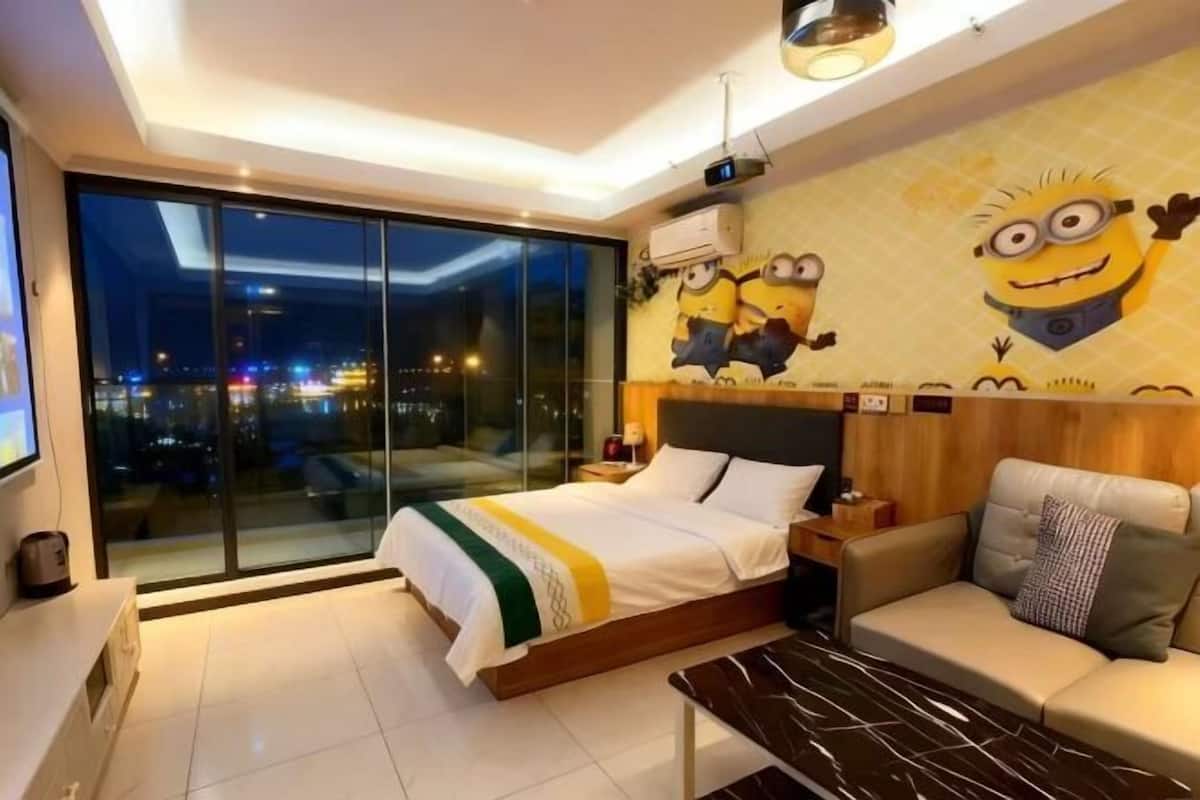 A modern hotel room with a large bed, a sofa, a coffee table, and a city view.