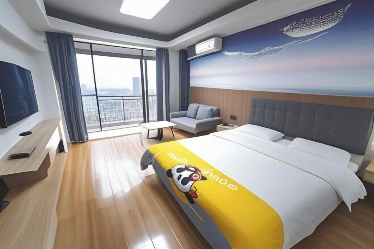 A hotel room with a bed, a sofa, a desk, and a large window with a city view.