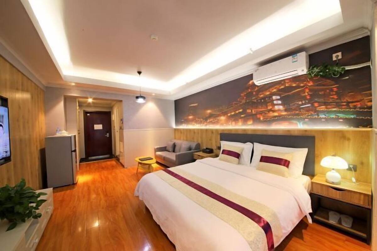 A hotel room with a large bed, a nightstand, a TV, and a wall-mounted air conditioner.