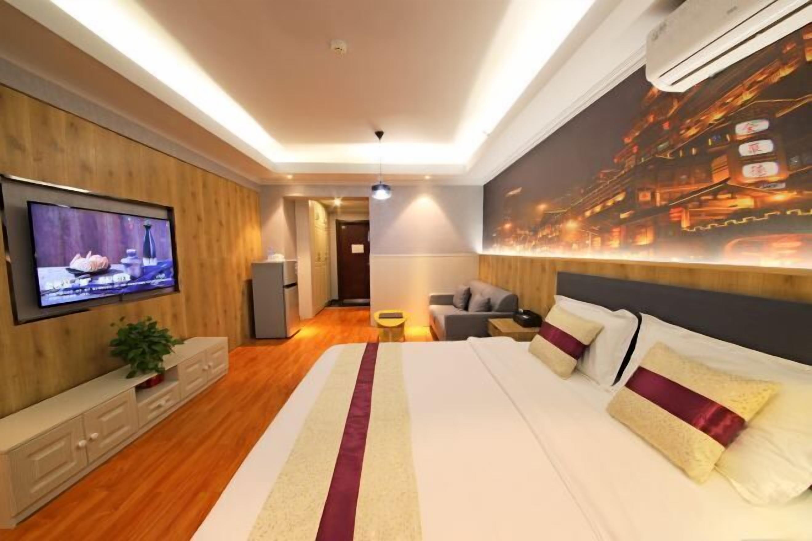 A modern hotel room with a large bed, a flat-screen TV mounted on the wall, a sofa, and a dining table.