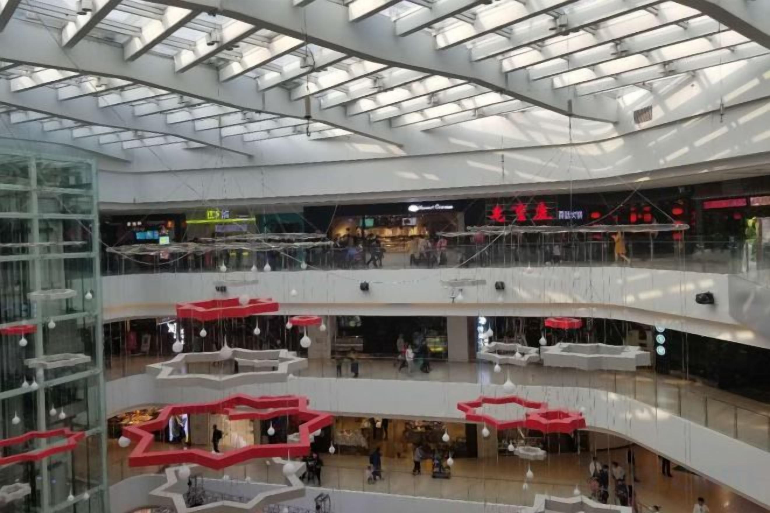 Ein mehrgeschossiges Einkaufszentrum mit Glasgeländern, schwebenden roten Sitzbereichen und verschiedenen Geschäften.