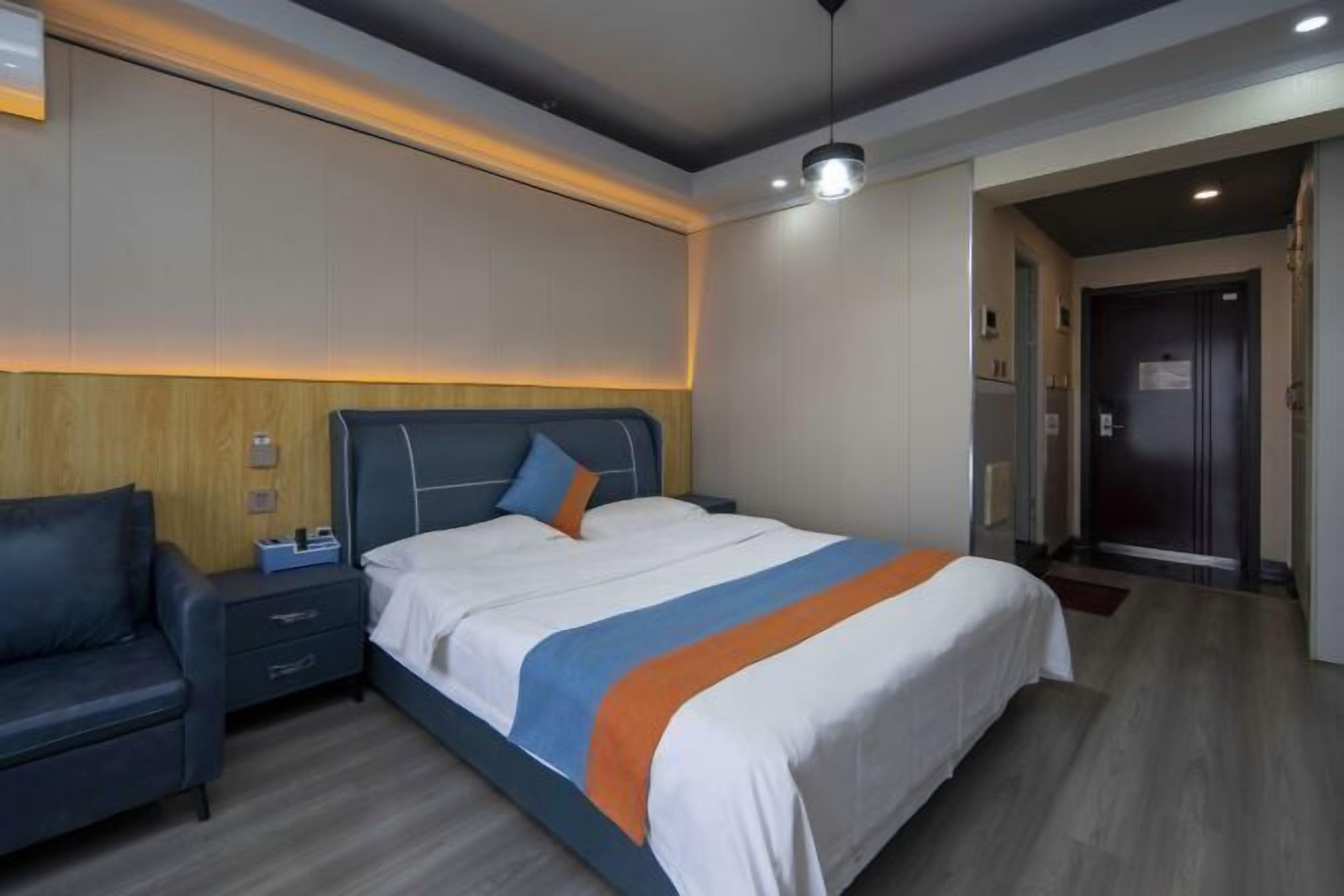 A modern hotel room with a large bed, a bedside table, a chair, and a wooden accent wall.