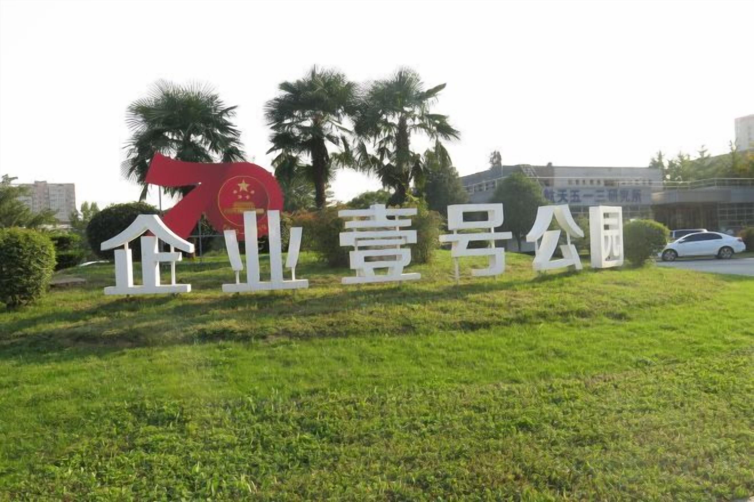 A grassy area with a large red and white sign, palm trees, and a building in the background.