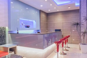 Un espace d’accueil moderne avec une cloison en verre, un comptoir d’accueil et des tabourets de bar rouges.