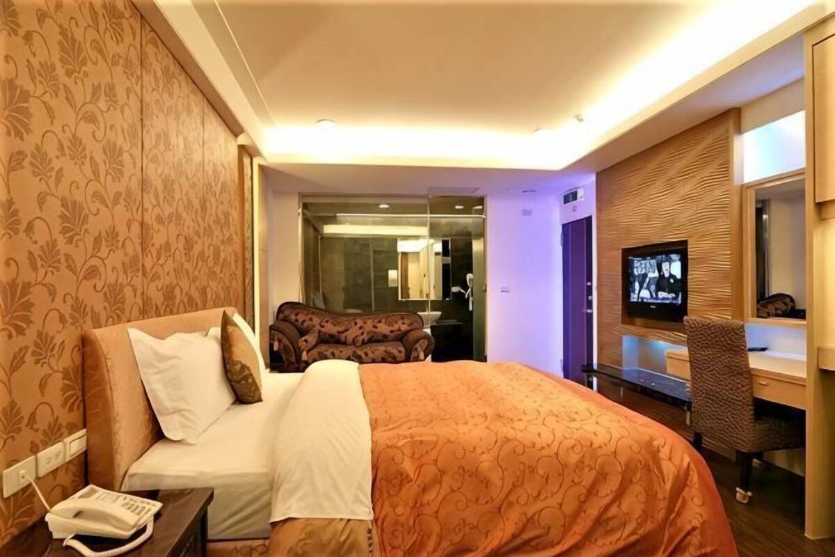 Hotellihuone, jossa on sänky, televisio, työpöytä ja peili.