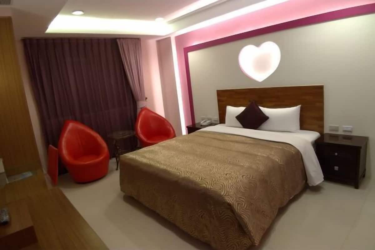 Hotellihuone, jossa on sänky, yöpöytä, punainen tuoli ja seinälle kiinnitetty sydämenmuotoinen valaisin.
