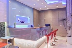 Una recepción moderna con un mostrador de vidrio, taburetes rojos y una planta.