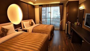 Habitación de hotel con dos camas, televisión, ventana grande con cortinas y televisión de pared.