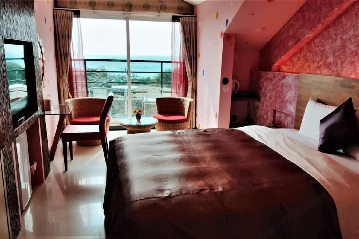 Hotellihuone, jossa on suuri sänky, televisio, parveke, jolta on näkymä merelle, sekä kaksi tuolia.