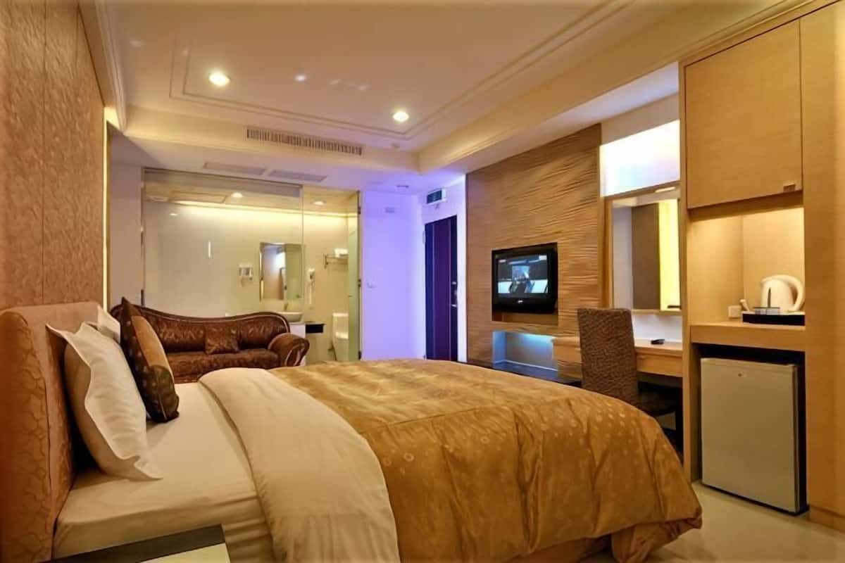 Hotellihuone, jossa on sänky, työpöytä, televisio ja pieni jääkaappi.