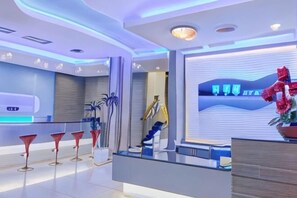 Un espace d’accueil moderne pour un hôtel, comprenant un comptoir d’accueil, un coin salon et des éléments décoratifs.