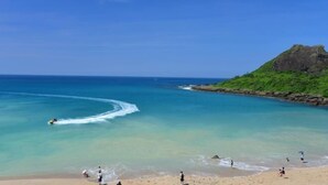 Una playa con agua turquesa cristalina, un promontorio rocoso y gente disfrutando de la orilla.
