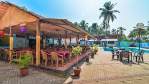 A covered outdoor dining area with wicker furniture and potted plants. - VISTA Montanha  GOA (Calangute)
