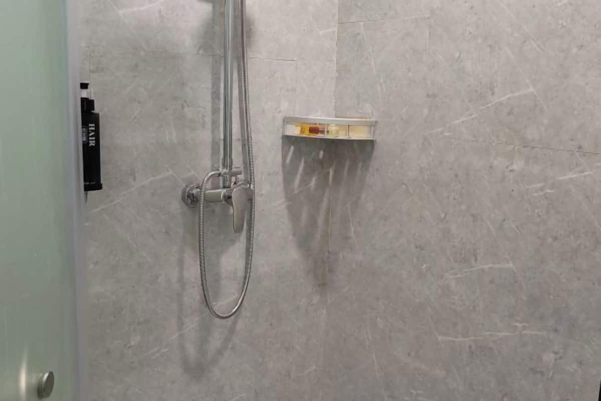 A shower with a handheld hose, a control panel, and a small shelf with toiletries.