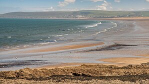 Une plage côtière avec un premier plan rocheux, des vagues et des bâtiments situés au loin.