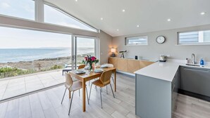 Une cuisine moderne dotée d’un grand îlot central, d’un coin repas offrant une vue sur l’océan et d’un plan de travail avec un évier et une horloge.