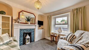 A cozy living room with a fireplace, a comfortable sofa, a television, and a window with curtains. - 2 Bed in Appledore (oc-s29561) (Appledore)