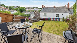 A patio with a round table and chairs, a small garden, and a colorful fence. - 2 Bed in Appledore (oc-s29561) (Appledore)