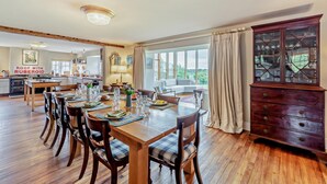 Uma sala de jantar espaçosa com uma mesa de madeira posta para seis pessoas, ladeada por cadeiras de madeira escura. Um armário de madeira grande com portas de vidro é visível à direita.