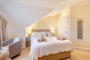 Um quarto com uma cama grande, duas mesas de cabeceira com luminárias, uma cadeira e uma porta.