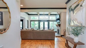 A spacious living room with a large sofa, wooden flooring, and a view through large windows. - Amazing Estate right on the lake, 2 homes, sleeps 28.  Arcade room, private dock (Appling)