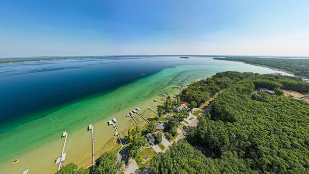 An aerial view of a coastal area with clear waters, a dock, and a row of houses adjacent to the beach. - Sandy Bottoms....Higgins Lake 3 bedroom + Detached Bunkhouse (Roscommon)