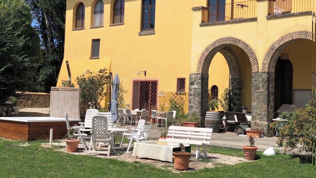 Ein gelbes Gebäude mit Rundbogenöffnungen und einer Terrasse mit Gartenmöbeln.
