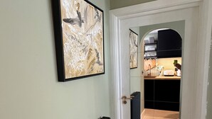 A hallway with a radiator, a framed abstract painting, and a view into a kitchen through an archway.