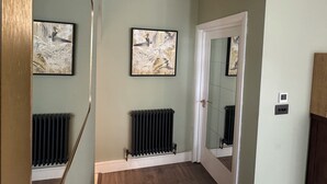 A hallway with two framed abstract paintings, a radiator, and a door with a mirror reflecting the room.