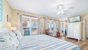 A bedroom with a large bed, a ceiling fan, a TV, and a guitar.