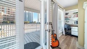 A room with a balcony, a guitar, a desk, and a bookshelf.