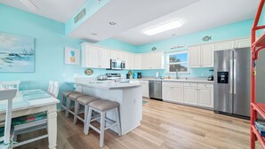 A modern kitchen with white cabinets, a stainless steel refrigerator, and a central island with stools.