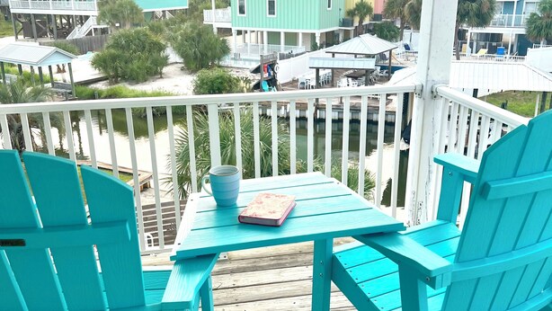 A turquoise deck with a table and chairs, overlooking a waterfront with colorful buildings.