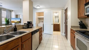 Une cuisine moderne équipée d’un évier à deux bacs, d’un lave-vaisselle et d’une cuisinière. Un four à micro-ondes est installé au-dessus de la cuisinière et une machine à café se trouve sur le plan de travail.