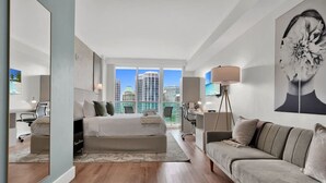 A modern hotel room with a large bed, a sofa, a desk, and a view of the cityscape.