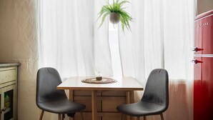 Ein Zimmer mit Holztisch, zwei schwarzen Stühlen, einem Topf mit Pflanze, einem weißen Vorhang und einem roten Schrank.