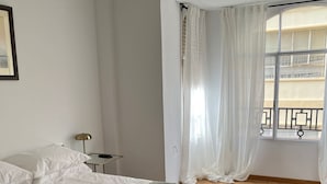 A bedroom with a bed, a nightstand, a lamp, and a window with curtains.