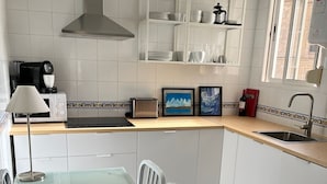 A modern kitchen with white cabinets, a stainless steel range hood, a coffee maker, and a toaster. There is a dining table with chairs and a window with a view.