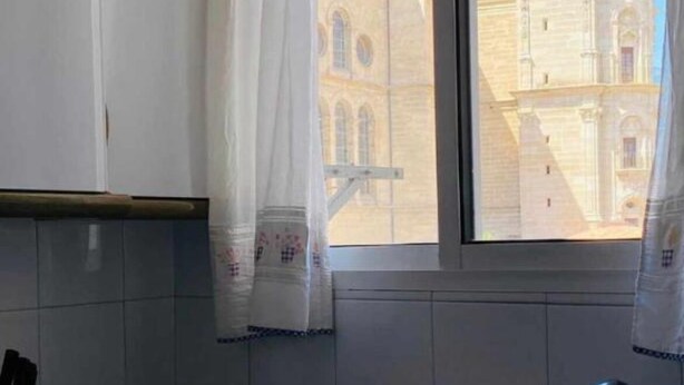 A room with a view of a historical building with a dome through a window with white curtains.