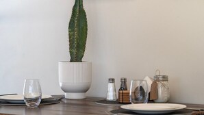 Une table à manger dressée avec des assiettes, des verres, un cactus dans un pot blanc, des salières et des poivrières, et un bocal muni d’une étiquette.