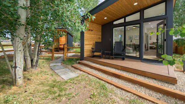 Un bâtiment moderne doté d’une terrasse en bois, de grandes portes vitrées et d’un petit espace extérieur aménagé pour s’asseoir.