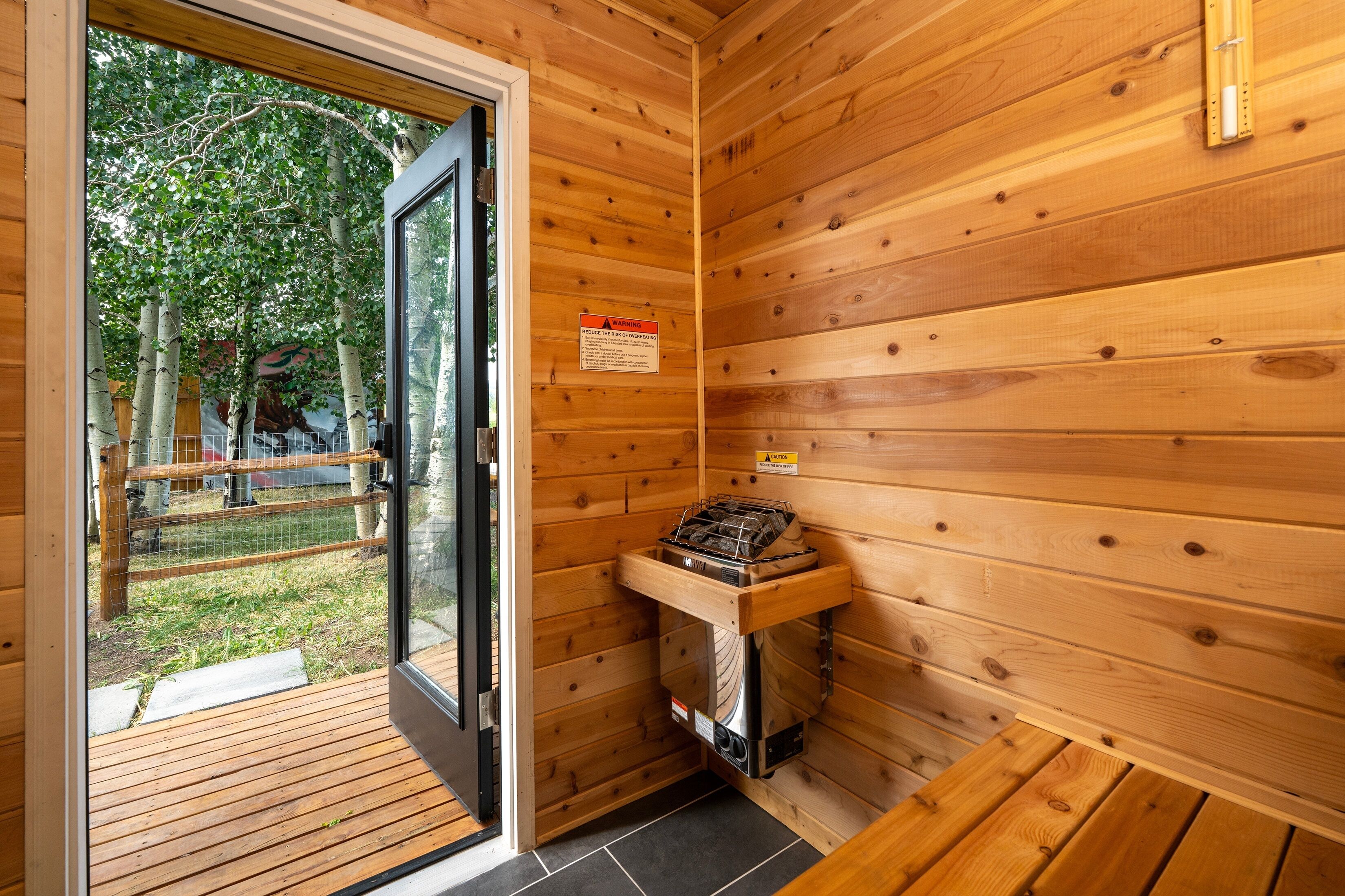Interieur van een houten chalet met een glazen deur naar buiten, een ingebouwde houtkachel en een waarschuwingsbord aan de muur.