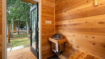 Interieur van een houten chalet met een glazen deur naar buiten, een ingebouwde houtkachel en een waarschuwingsbord aan de muur.