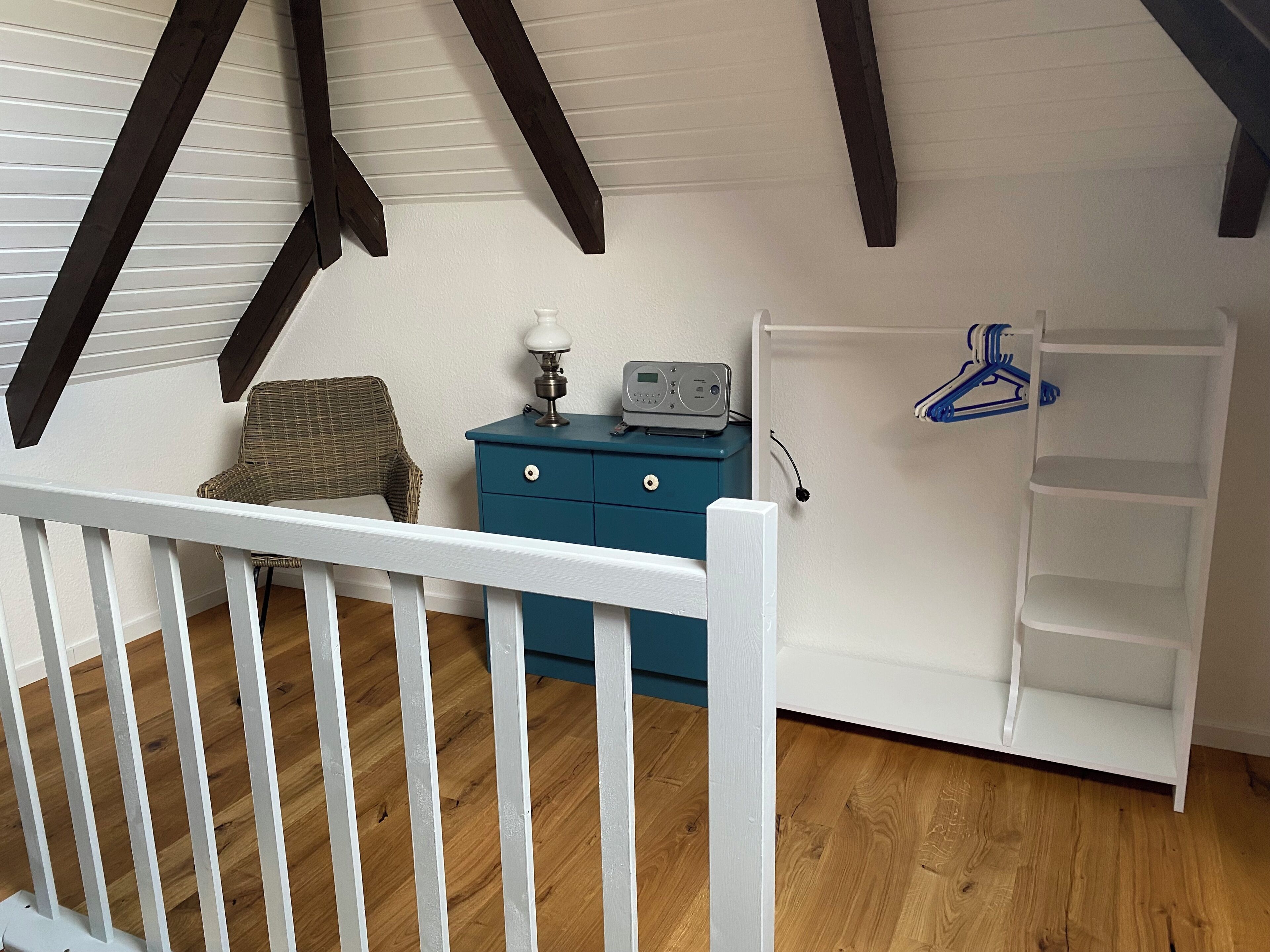 Une pièce avec un berceau blanc, une commode bleue, un fauteuil en osier et une étagère blanche.