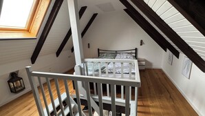 A room with a sloped ceiling, a crib, a bed, a small table, and a window. - Maisonette-wohnung mit Schönem Balkon in Deichnähe (Friedrichskoog)