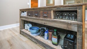 A kitchen with a wooden shelf holding various kitchen items, including bowls, a toaster, and a bottle of olive oil.