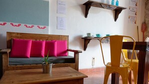 A room with a wooden sofa, a small table, a yellow chair, a shelf with blue bottles, and a wall with text and a red border. - Estudio `Centro histórico  Morelia Michoacan` (Morelia)
