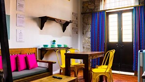 A room with a wooden table, yellow chairs, a sofa with pink cushions, a black door, and a window with blue curtains. - Estudio `Centro histórico  Morelia Michoacan` (Morelia)