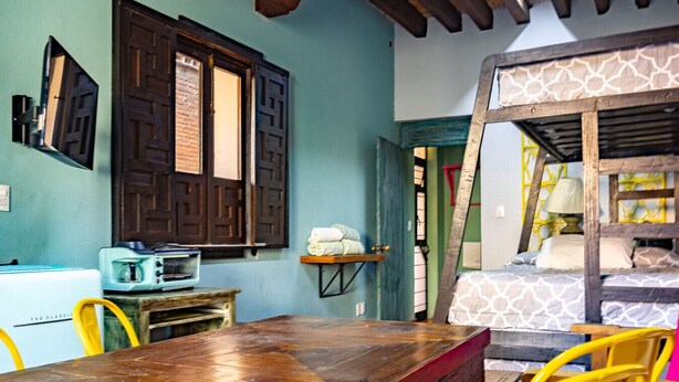 A rustic room with a wooden table, a vintage radio, a bed with patterned bedding, and a ladder leading to a loft. - Estudio `Centro histórico  Morelia Michoacan` (Morelia)