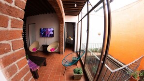 Un balcon abrité équipé d’un téléviseur, de fauteuils en osier et de plantes en pot.